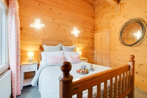A wooden cabin bedroom with a bed, bedside lamps, a mirror, and a window with curtains.