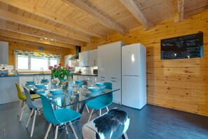 Eine moderne Küche mit Holzwänden, einem Glastisch, blauen Stühlen und einer Tafel als Speisekarte.