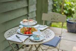 Ein Tisch mit einem dreistöckigen Kuchenstand, Erdbeeren auf einem Teller und einer Tasse auf einer Terrasse.