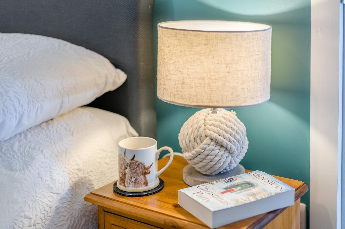 Ein Nachttisch mit einer Lampe, einer Tasse und einem Buch.