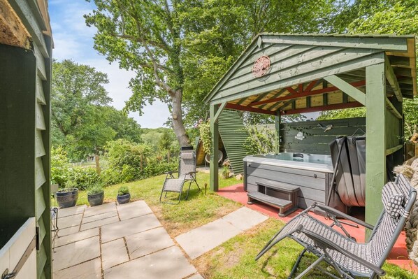 Eine überdachte Terrasse im Freien mit Whirlpool, Sitzgelegenheit und Topfpflanzen.