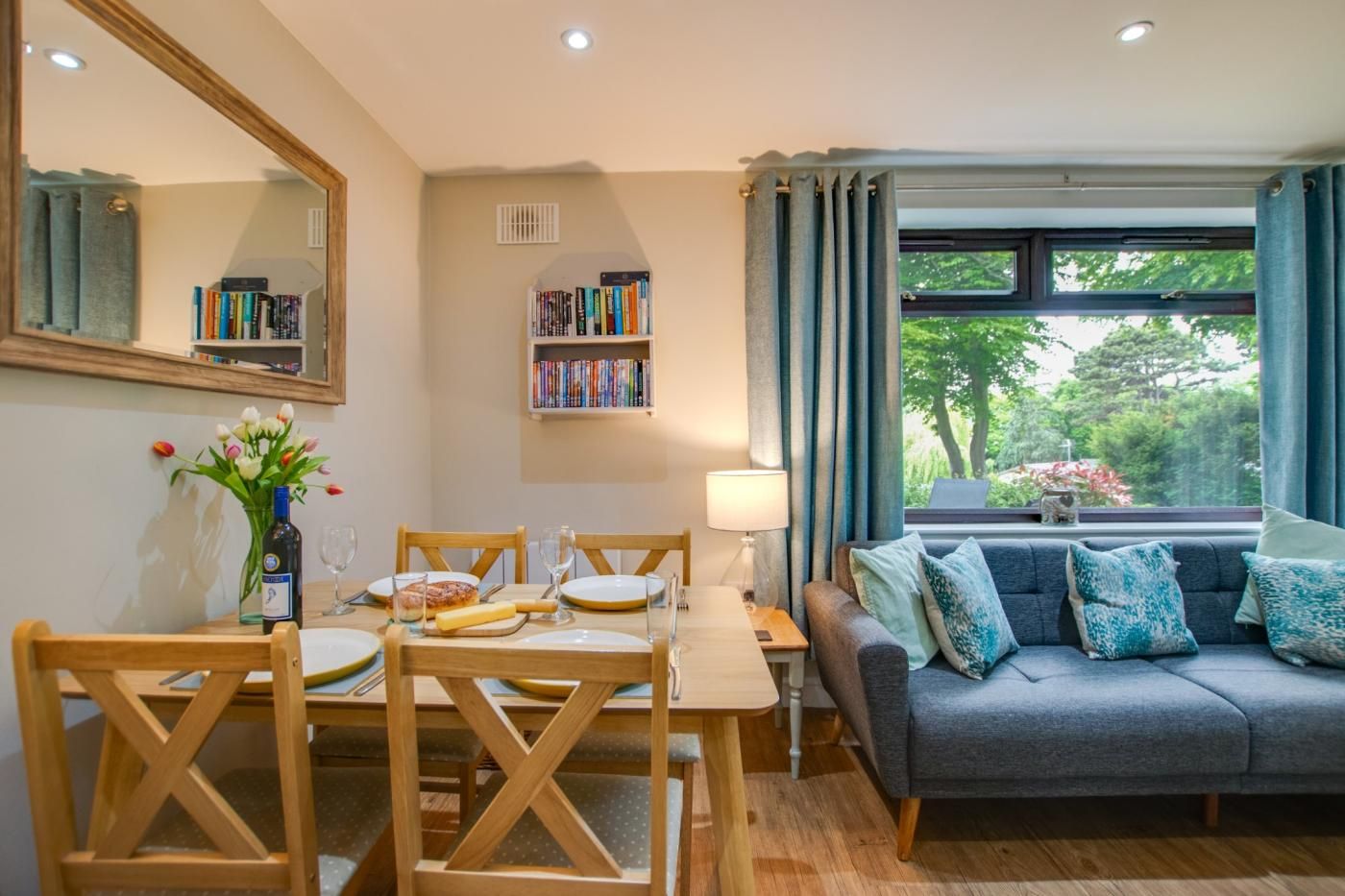 A dining area with a table set for two, a sofa, and a bookshelf with books.