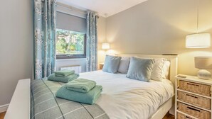Un lit bien fait, avec des oreillers et des serviettes pliées, une table de chevet avec une lampe et une fenêtre avec des rideaux.