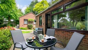 Une terrasse avec une table ronde, deux chaises et, en arrière-plan, un bâtiment en briques.