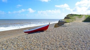 Une plage de galets avec un bateau rouge et un sentier menant à une zone herbeuse.