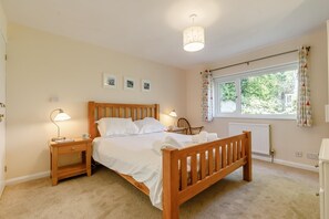 A bedroom with a wooden bed, bedside lamps, a window with curtains, and a radiator. - 3 Bed in Wadebridge (oc-p00427) (Little Petherick)