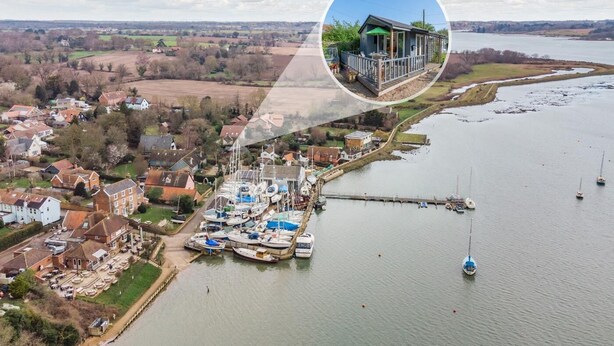 An aerial view of a riverside village with a marina, houses, and a small dock.