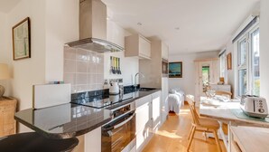 A modern kitchen with a central island, a dining area with a table and chairs, and a view of the outdoors through large windows.