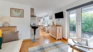 A modern kitchen with a central island, a dining area with a table and chairs, and a large sliding glass door leading to a garden.