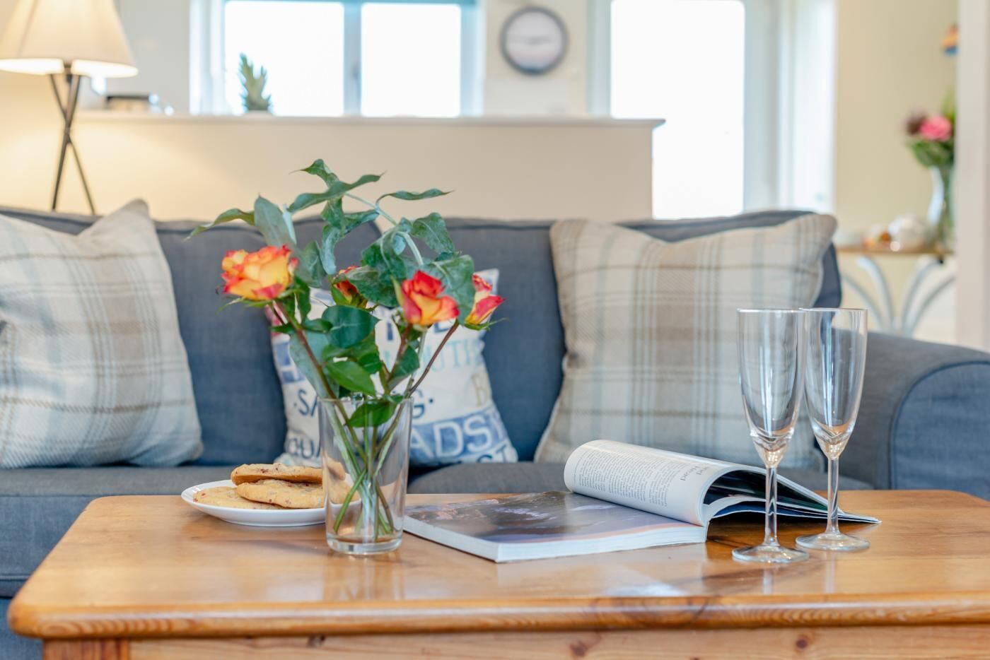 A cozy living room with a sofa, a coffee table, a vase with flowers, a plate of cookies, and two glasses.