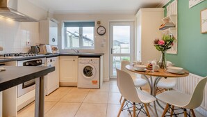 A modern kitchen with a stove, oven, washing machine, and a dining area with a table and chairs.