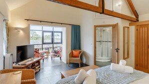 A spacious bedroom with a large bed, a TV, a seating area with a table and chairs, and a shower room. - 3 Bed in Wadebridge (oc-p00421) (Saint Issey)