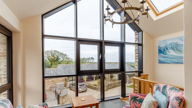 A spacious room with large windows, a modern chandelier, and a view of the outside. - 3 Bed in Wadebridge (oc-p00421) (Saint Issey)