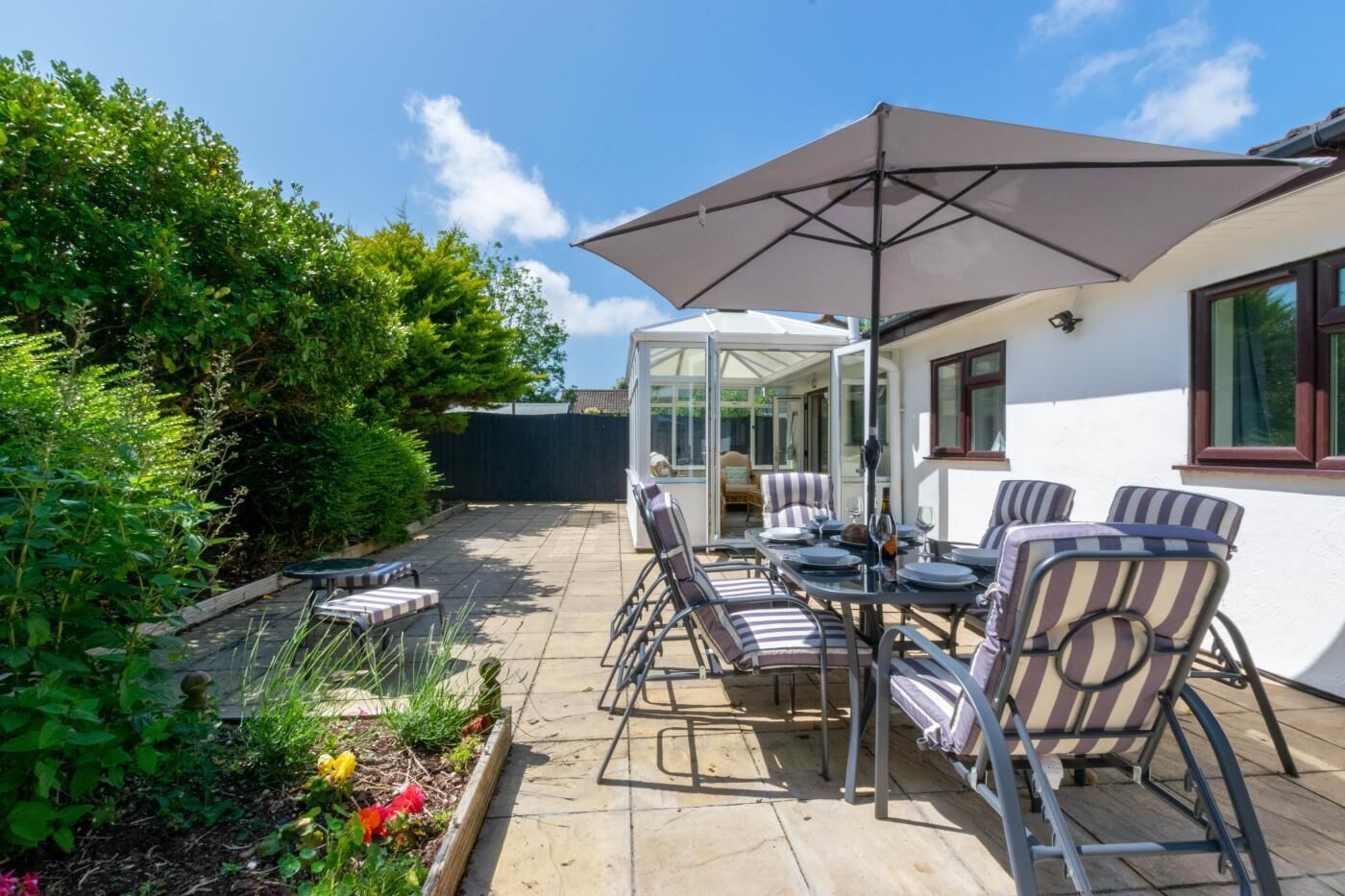 A patio with a table and chairs, a glass enclosure, and a view of a garden.
