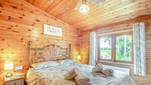 A wooden cabin bedroom with a bed, bedside table, lamp, and window with curtains.