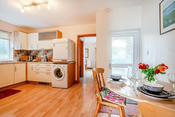 A compact kitchen with a washing machine, a dining area with a table set for two, and a view of the outdoors.