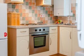 A kitchen with a stove, oven, and a fruit bowl on the counter.