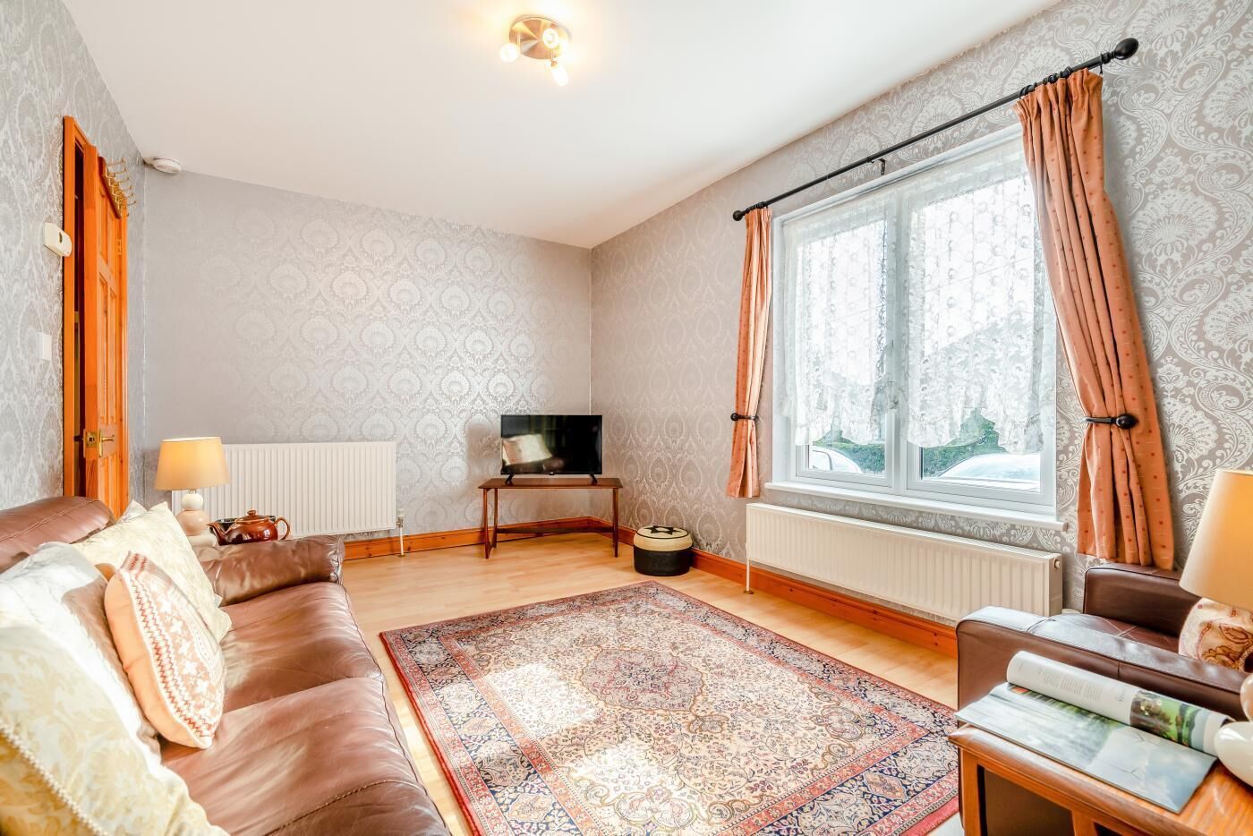 Un salon avec un canapé, un téléviseur, une fenêtre avec des rideaux et un tapis à motifs.
