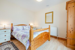 A bedroom with a wooden bed, a nightstand, a dresser, a radiator, and a wardrobe.
