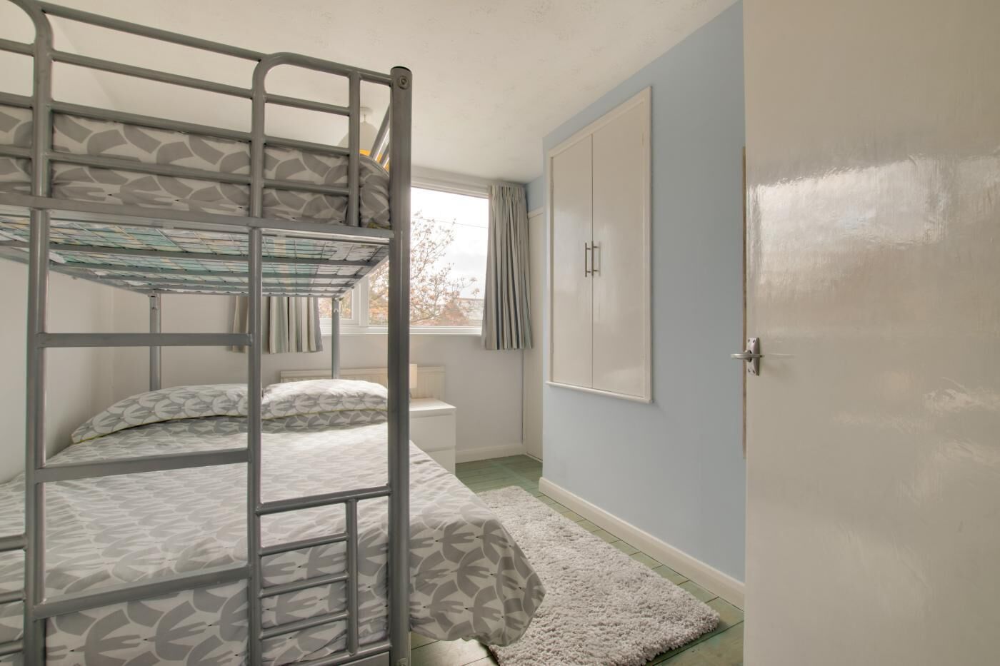 A bunk bed room with a window, a white radiator, and a door.