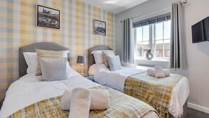 A hotel room with two beds, a window with curtains, a flat-screen TV, and two framed pictures on the wall. - 2 Bed in Whitby (oc-w1008) (Whitby)