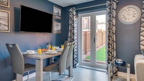 A modern dining area with a table set for breakfast, a television mounted on the wall, and a clock on the wall. - 2 Bed in Whitby (oc-w1008) (Whitby)