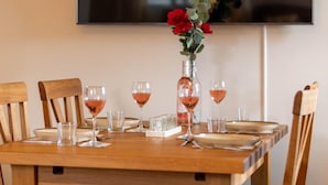 A dining table set with wine glasses, a vase with red flowers, and a bottle of wine. - 3 Bed in Bainbridge (oc-ds1026) (Bainbridge)