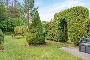 Ein gepflegter Garten mit ordentlich geschnittenen Hecken, einem Picknicktisch und einer Bank.