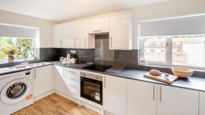 A modern kitchen with white cabinets, a black countertop, a built-in oven, and a window with a view of the outside. - 3 Bed in Morpeth (oc-t32249) (Thirston)