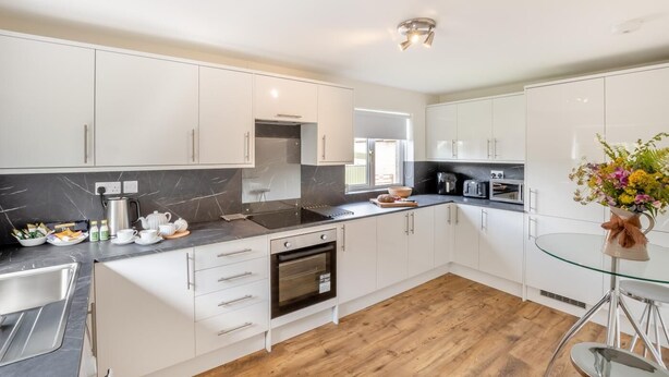 A modern kitchen with white cabinets, a black countertop, and a wooden floor. - 3 Bed in Morpeth (oc-t32249) (Thirston)