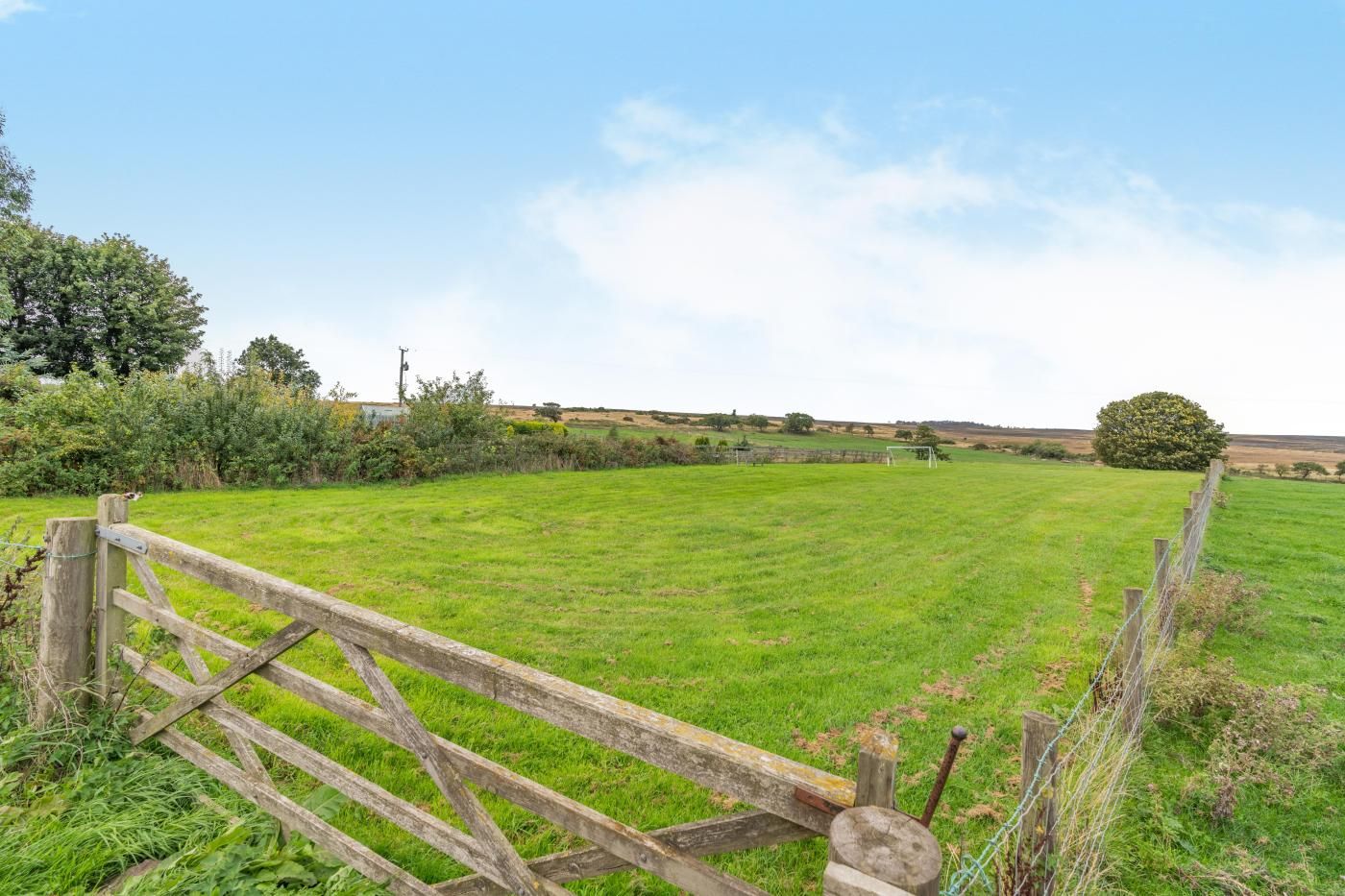 A grassy field with a wooden gate and a metal fence.