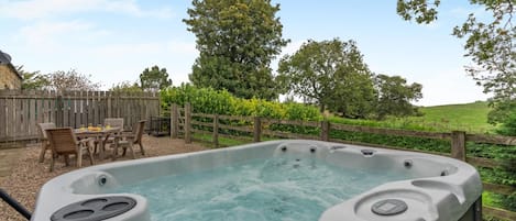 A hot tub with a wooden deck and chairs, surrounded by a wooden fence and greenery.