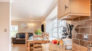 Eine moderne Küche mit Holzschränken, einem Esstisch für vier Personen und Blick in das Wohnzimmer.