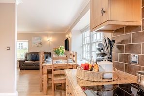 A modern kitchen with wooden cabinets, a dining table set for four, and a view into the living room. - 3 Bed in Whitby (oc-w1007) (Whitby)