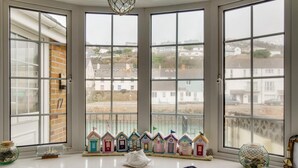 Et værelse med karnap der kigger ud over et kystområde, med en række farverige miniaturehuse på vindueskarmen.