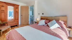 A bedroom with a large bed, wooden wardrobe, and a door leading to a dining area.