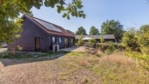 A rustic building with a sloped roof, a covered outdoor seating area, and a fenced garden.
