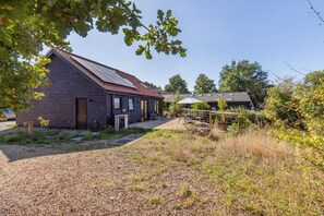 A rustic building with a sloped roof, a covered outdoor seating area, and a fenced garden.