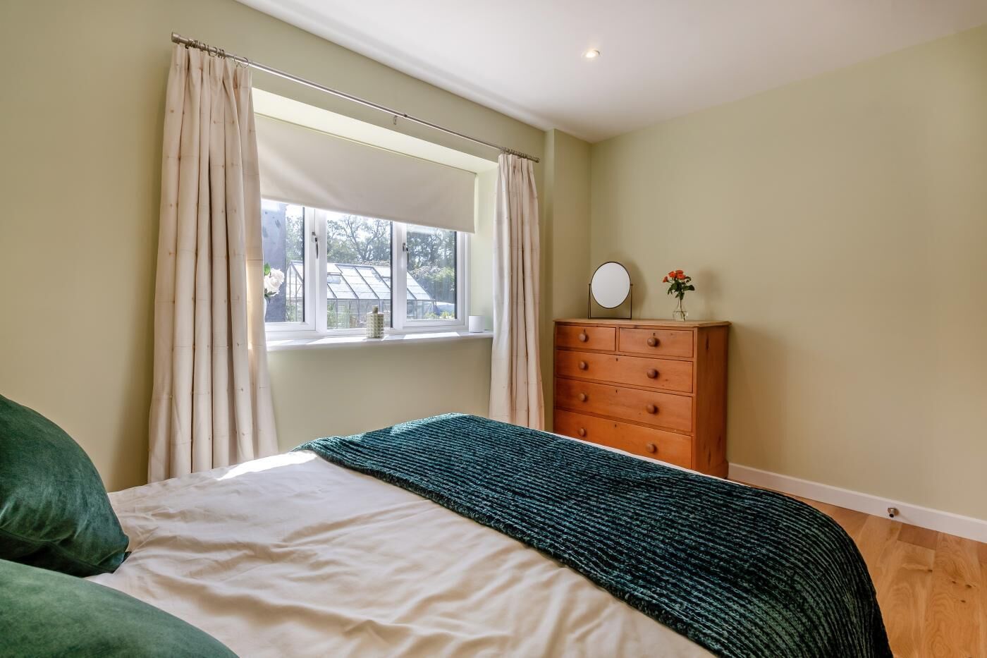 A bedroom with a bed, a dresser, a window with curtains, and a view of greenery outside.