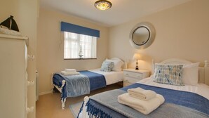 Una camera d'albergo con due letti, uno specchio rotondo, una finestra con tende e una lampada a sospensione.