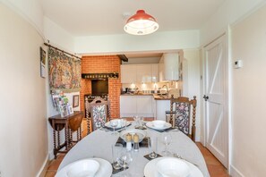 A dining area with a brick fireplace, a kitchen in the background, and a table set for four. - 3 Bed in Hastings (oc-h32649) (Three Oaks)