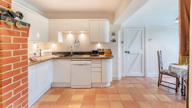 Una cucina compatta con mobili bianchi, lavastoviglie integrata e un piccolo isolotto con lavello.