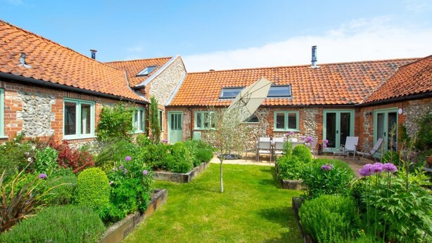 Een binnenplaats met een tuin, een stenen gebouw met een pannendak en een kleine boom.