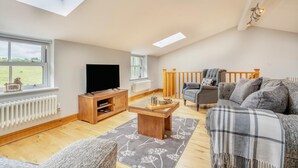A spacious living room with a high ceiling, a TV on a wooden stand, a grey sofa, and a wooden coffee table. - 2 Bed in Crook (oc-s32614) (Crook)