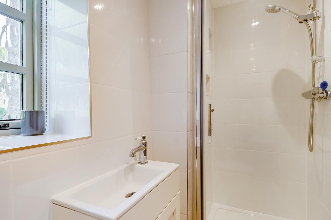 A bathroom with a white sink, a glass shower enclosure, and a window with a view.