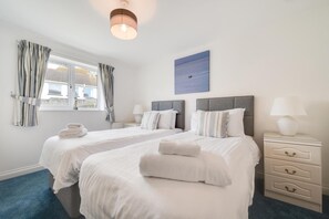 Ein Hotelzimmer mit zwei Betten, einem Fenster mit Vorhängen, einem Gemälde und einem Nachttisch mit Lampe.