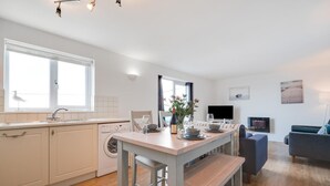 A modern kitchen with a dining area, a washing machine, and a flat-screen TV. - 2 Bed in Porthleven (oc-p00972) (Porthleven)