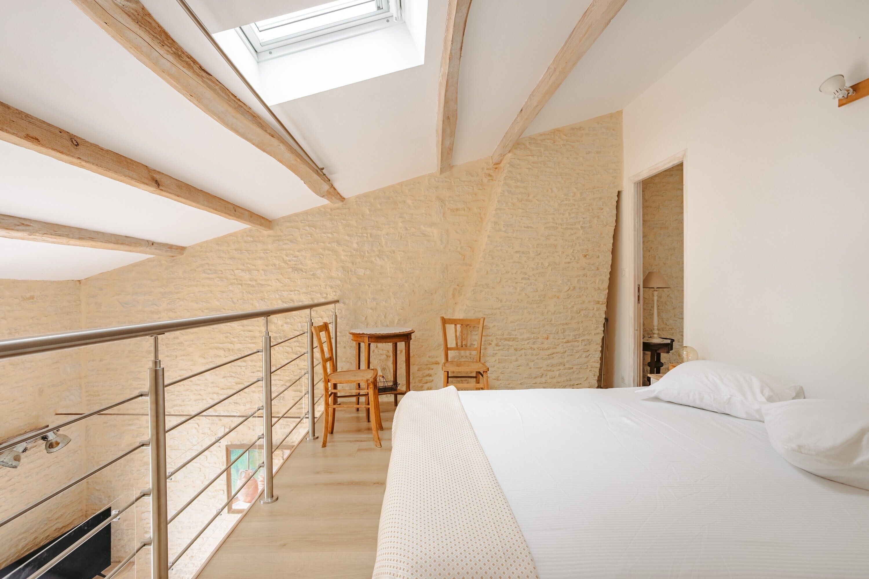 A bedroom with a skylight, a bed, a desk, and chairs.