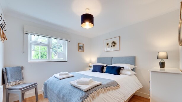 Quarto com cama, cadeira, mesa de cabeceira, abajur e janela.