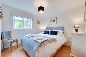Ein Schlafzimmer mit Bett, Sessel, Nachttisch, Lampe und Fenster.